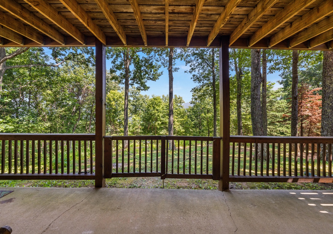 A peaceful covered deck overlooks lush forest scenery. Sunlight filters through the trees, creating a serene, private retreat where you can unwind and soak in nature.