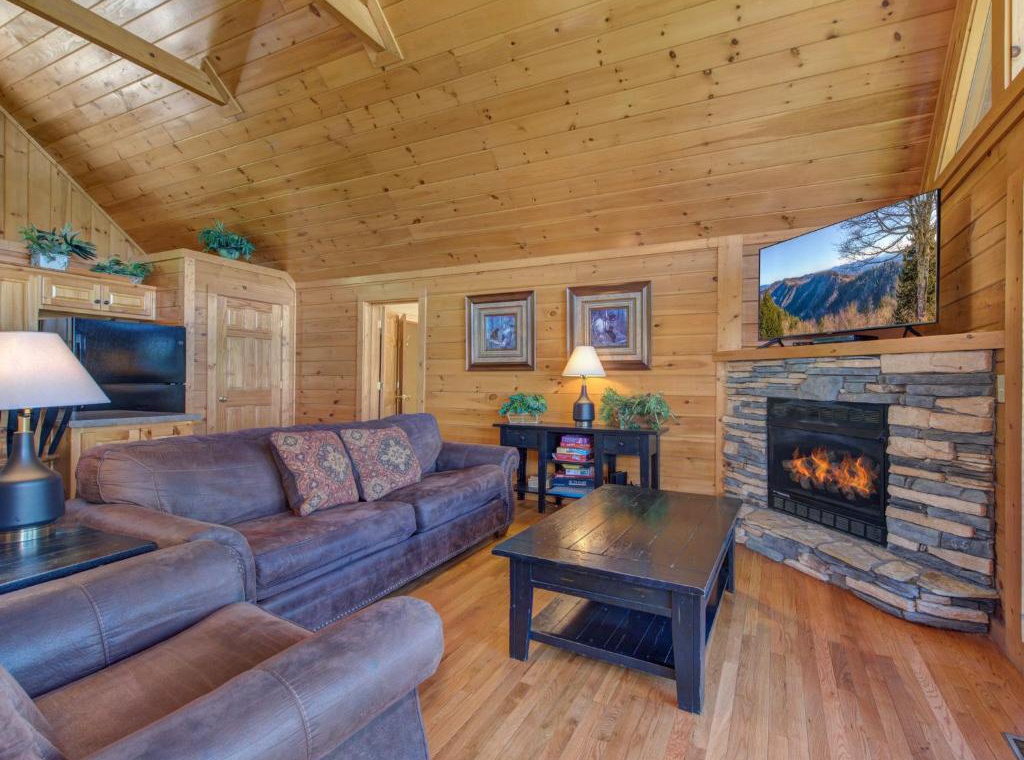 Cozy up in your rustic cabin living room with warm wood walls, crackling fireplace, and mountain views on the large screen.