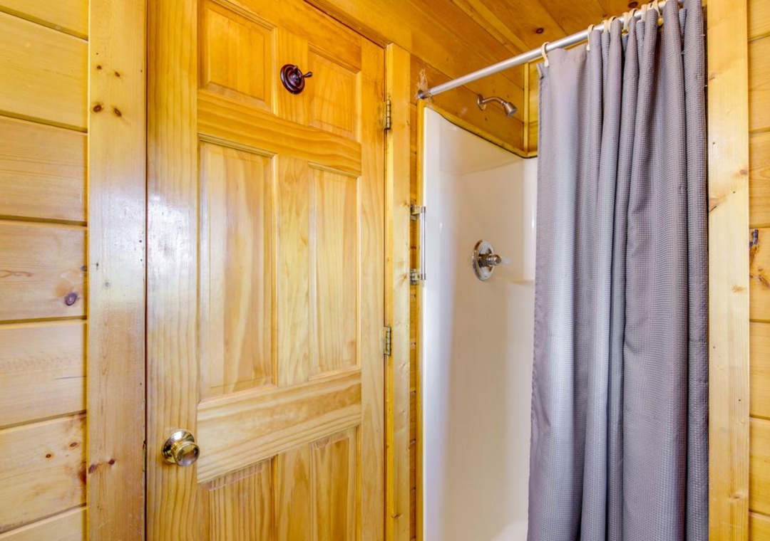 Step into your private rustic bathroom featuring warm pine walls and a refreshing shower with curtain for your comfort.