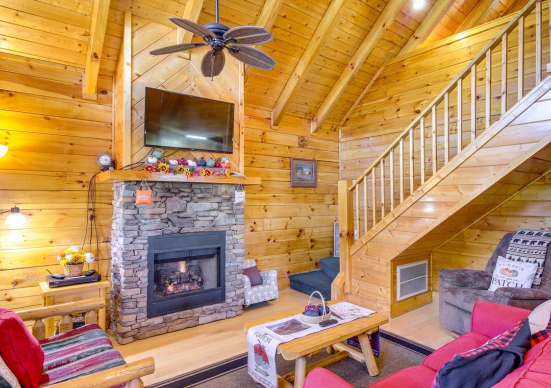 Unwind in your cozy living room featuring rustic log walls, stone fireplace, and comfortable seating perfect for relaxing evenings together.
