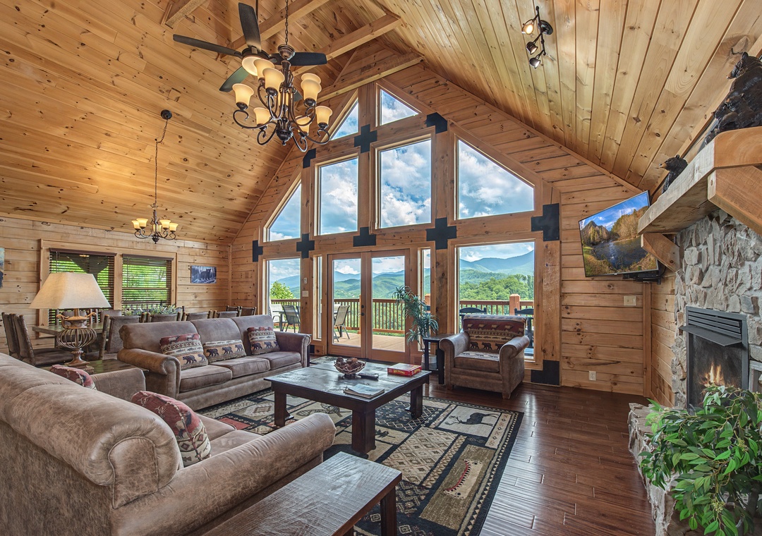 Unwind in this stunning cabin living room with soaring ceilings, warm wood paneling, and panoramic mountain views through expansive windows. Your perfect mountain escape awaits with a cozy fireplace and inviting seating for your group.