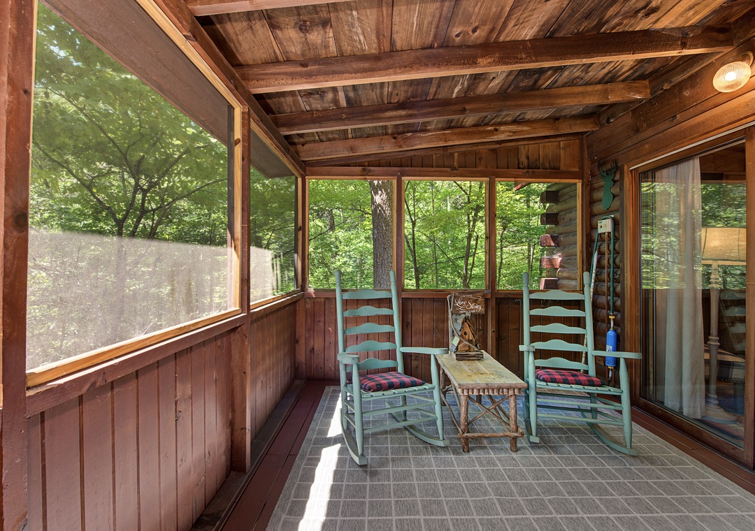 Step into your own screened porch retreat, where two rocking chairs invite you to unwind beneath rustic exposed beams. Surrounded by lush forest views, this cozy space feels like your private sanctuary for morning coffee or evening relaxation.