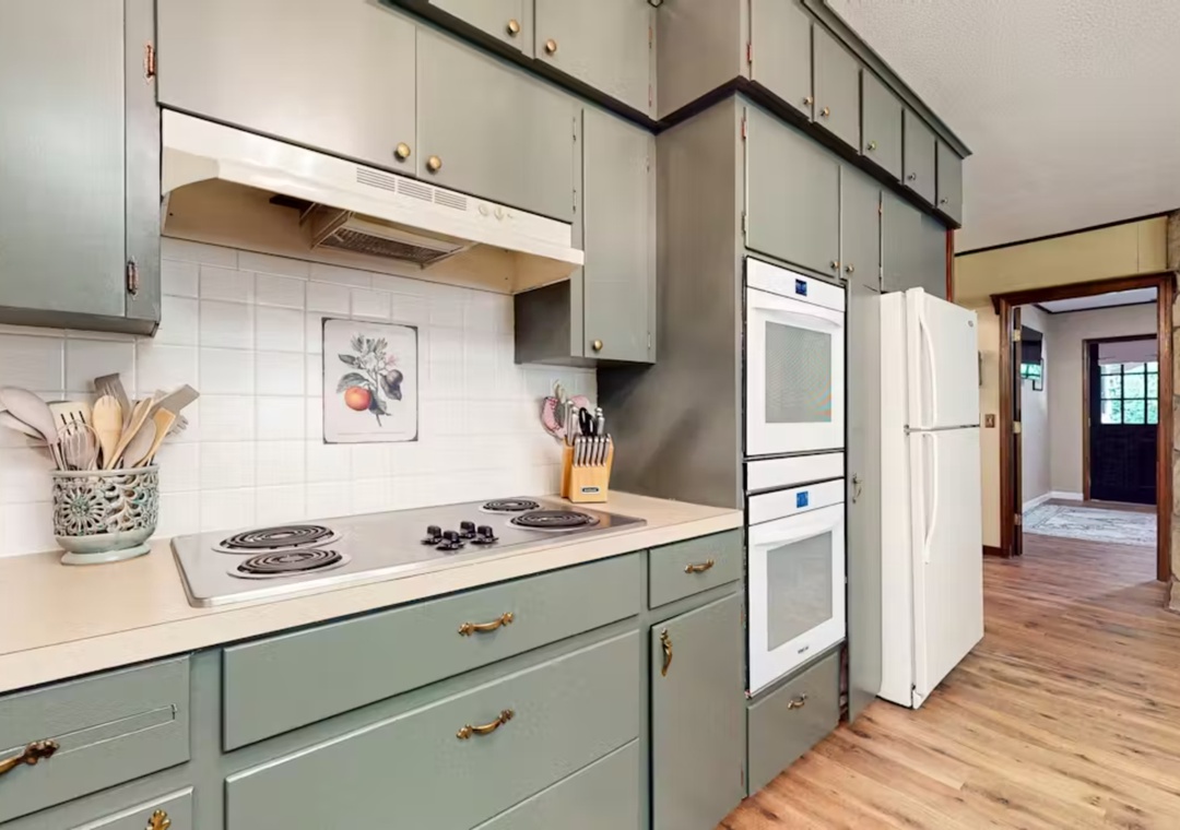 Your fully equipped kitchen invites culinary adventures with sage-green cabinets, modern appliances, and warm wood floors.