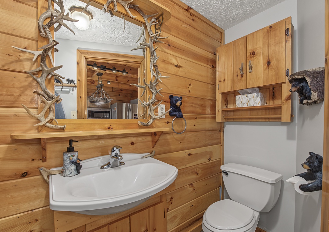 Rustic bathroom with charming woodland touches. Warm knotty pine walls and a unique antler-framed mirror create a cozy, cabin-style retreat just for you.