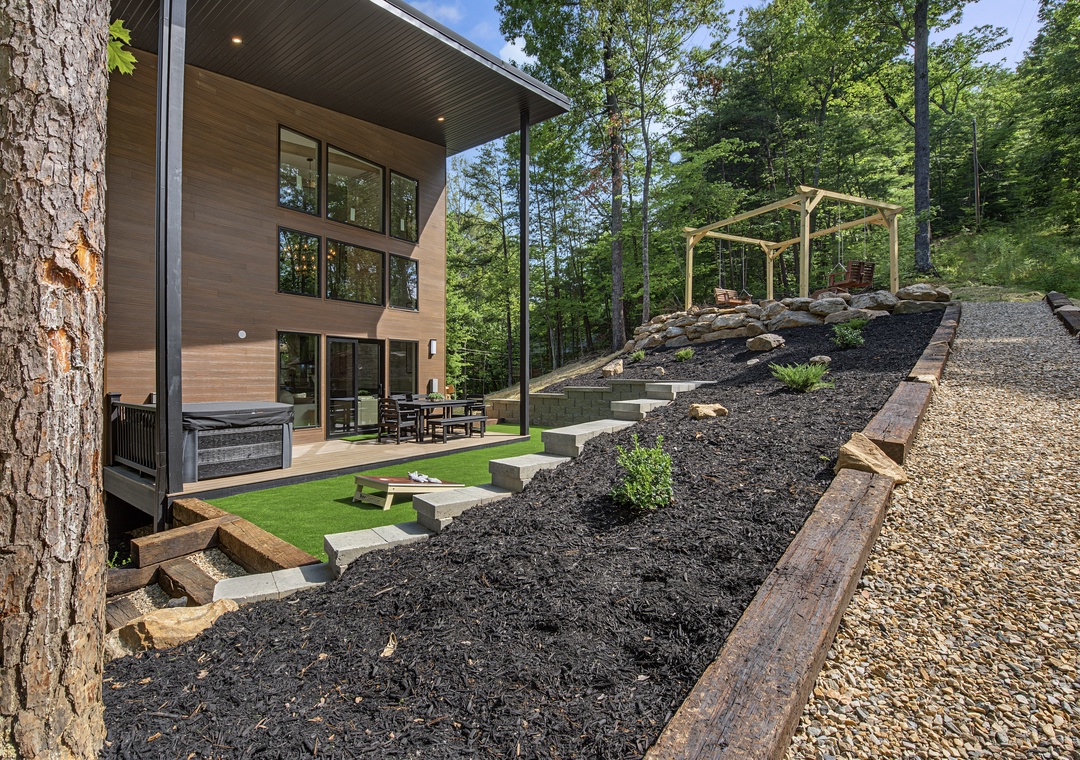 A modern retreat nestled in the woods with landscaped terraces, covered outdoor seating, and a pergola framing peaceful woodland views.