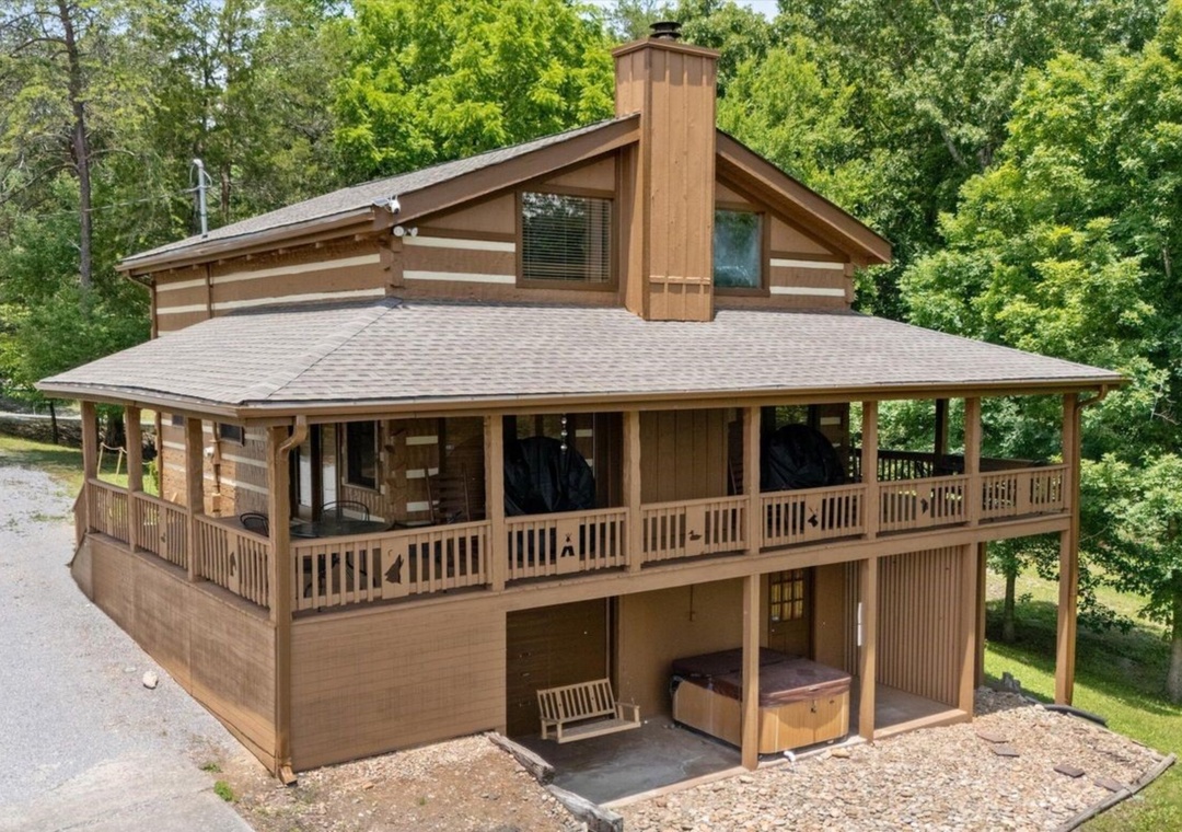 Rustic log cabin nestled among towering trees offers mountain retreat charm with wrap-around deck and lower-level hot tub relaxation area.