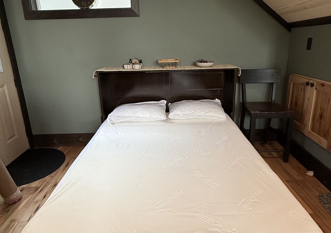 Your cozy attic retreat features exposed beams, soft sage walls, and a comfortable bed beneath a charming skylight.