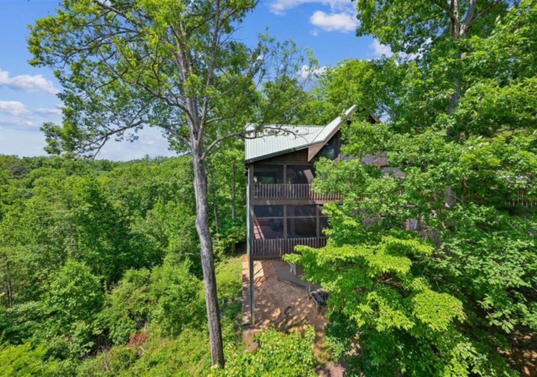 A secluded mountain cabin nestled among lush forest, featuring multiple balconies and a metal roof, set in a peaceful wooded hillside location.