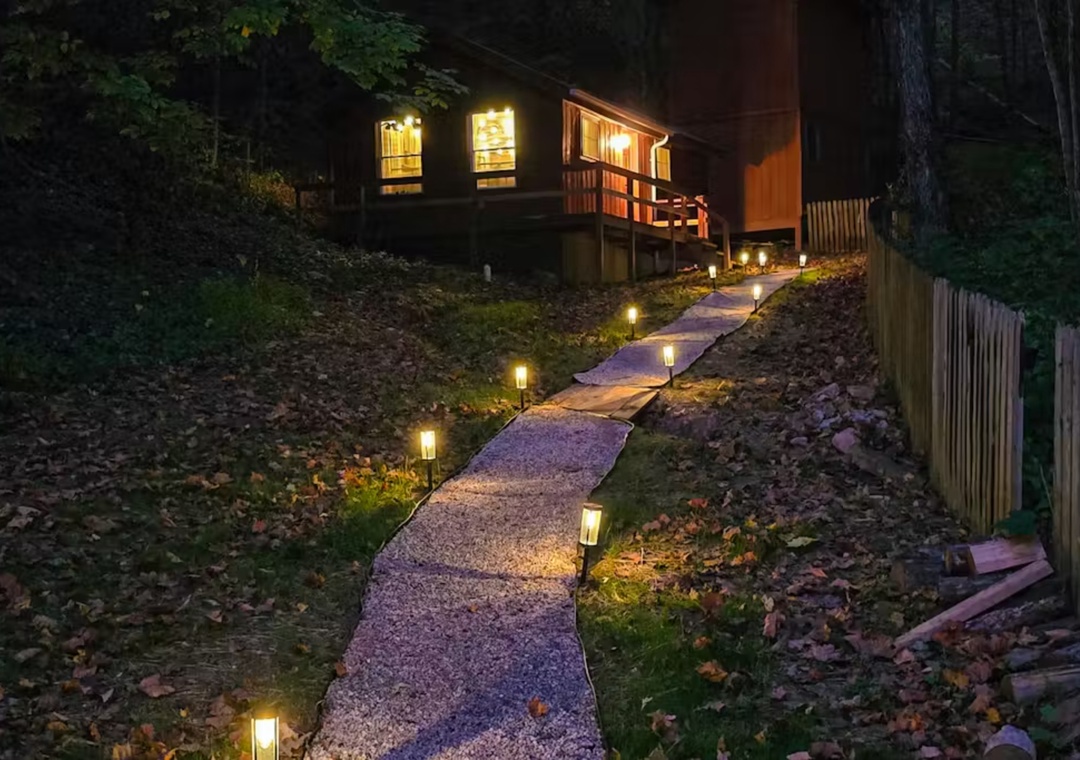 A warmly lit retreat nestled among towering trees, with illuminated pathways guiding your evening arrival to this cozy woodland escape.