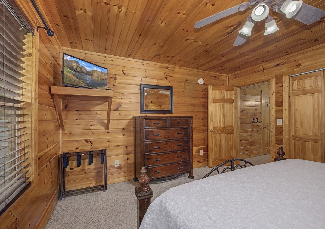 Unwind in your cozy cabin bedroom with warm wood-paneled walls, rustic furnishings, a flat-screen TV, and a ceiling fan for your comfort. Two doors offer private access to your retreat.