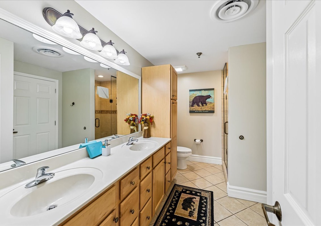 Spacious bathroom with dual sinks, warm wood cabinets, and thoughtful touches like fresh flowers to make your morning routine feel luxurious.