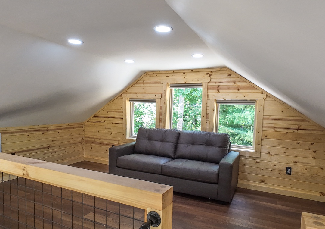 Settle into your charming loft space with warm wood accents and natural light pouring through forest views. The cozy sofa invites you to unwind after a day of exploration.