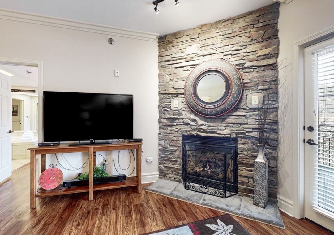 Unwind in your cozy living space featuring a stunning stone fireplace and modern TV entertainment area.