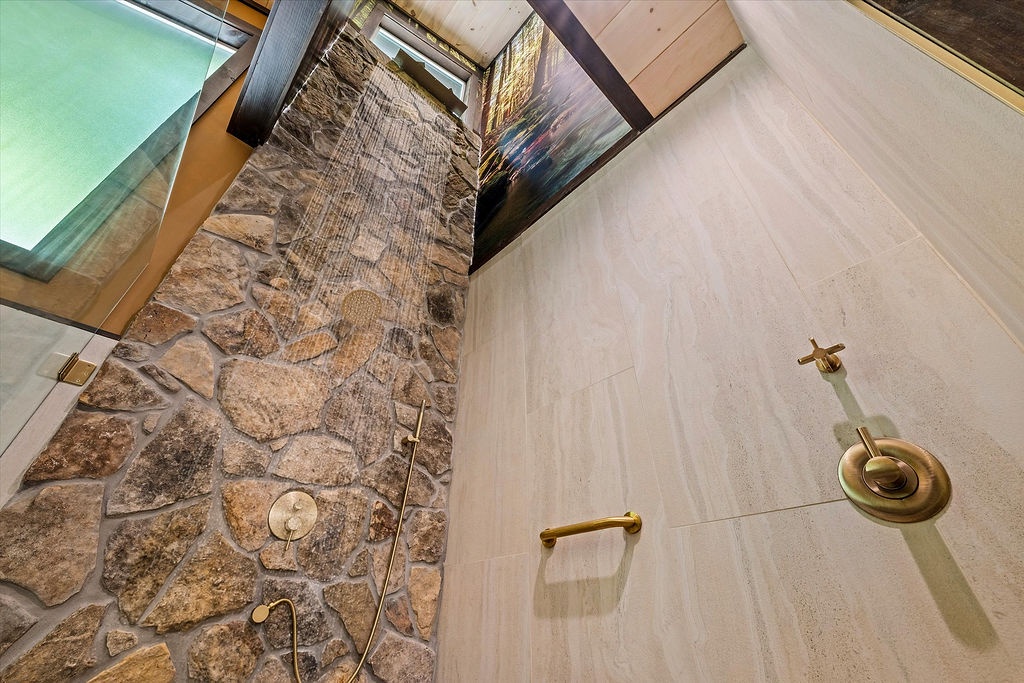 Unwind in your spa-like shower with elegant gold fixtures, natural stone accent wall, and sleek modern tile creating a serene retreat.