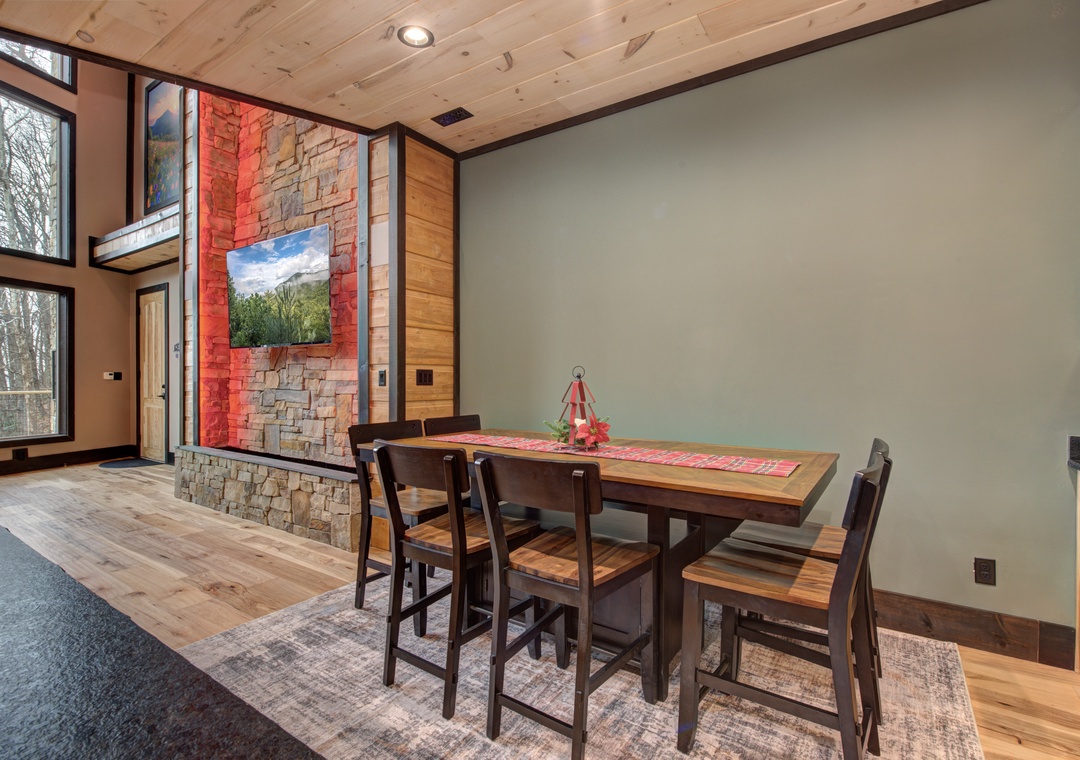 Gather around your elegant dining table surrounded by warm wood and stone, with stunning forest views through expansive windows.