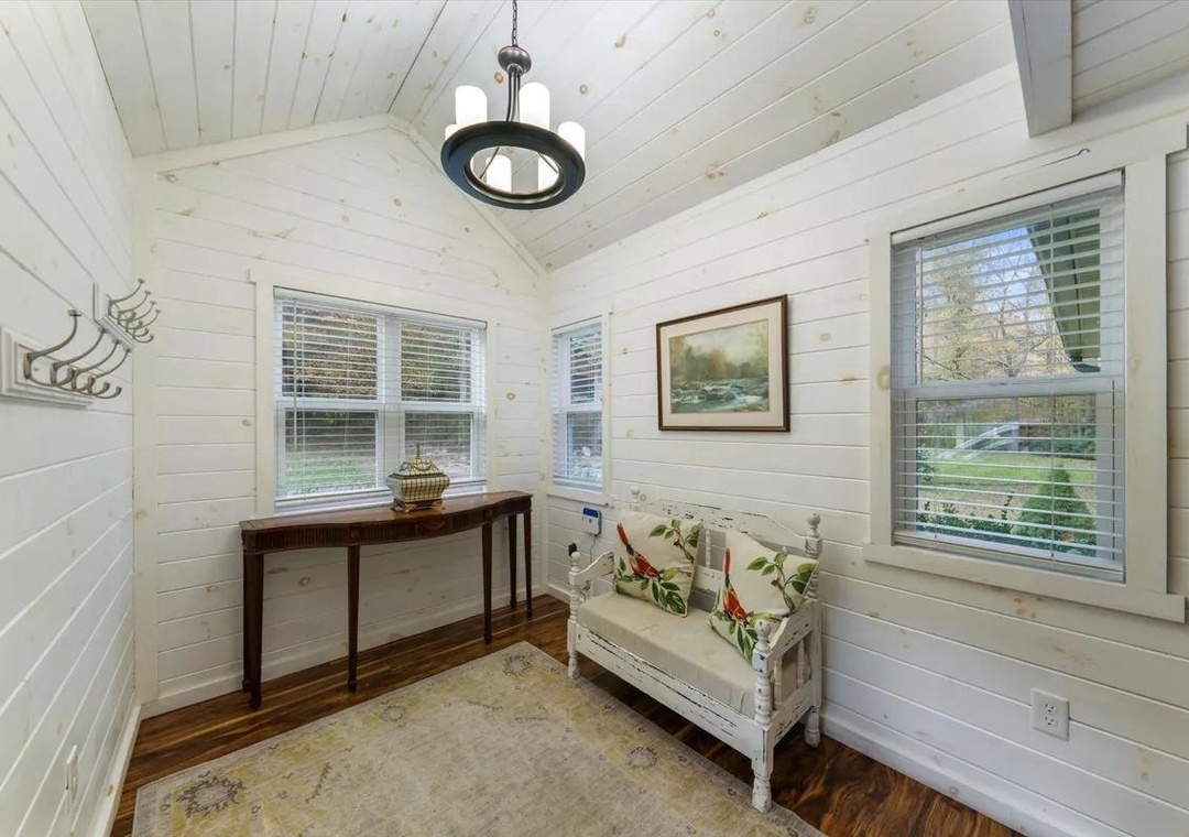 Step into your cozy nook, where natural light pours through large windows and crisp white shiplap walls create a serene retreat. Settle onto the charming bench with cheerful pillows and enjoy the peaceful garden views.