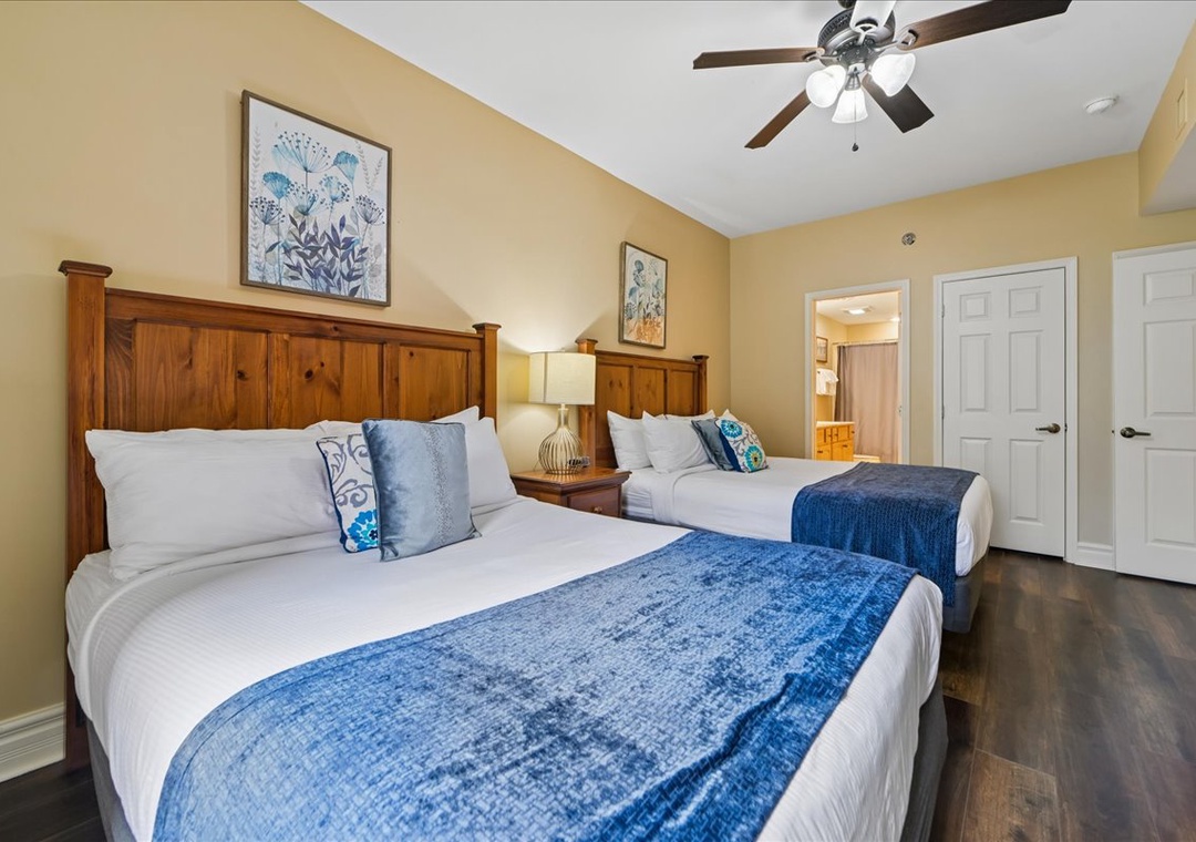 Your cozy bedroom features two comfortable beds with crisp linens, warm wood accents, and gentle ceiling fan keeping you cool.
