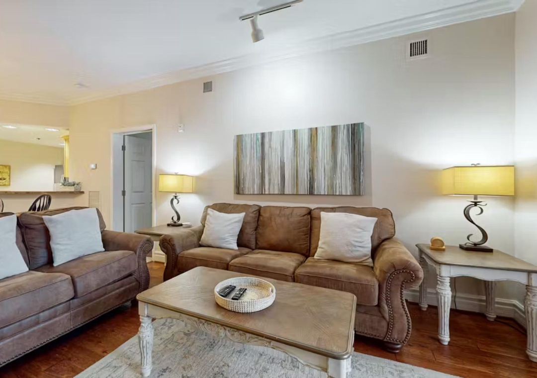 Sink into plush leather sofas in your elegant living space, where warm lighting and coastal artwork create the perfect atmosphere for relaxation.