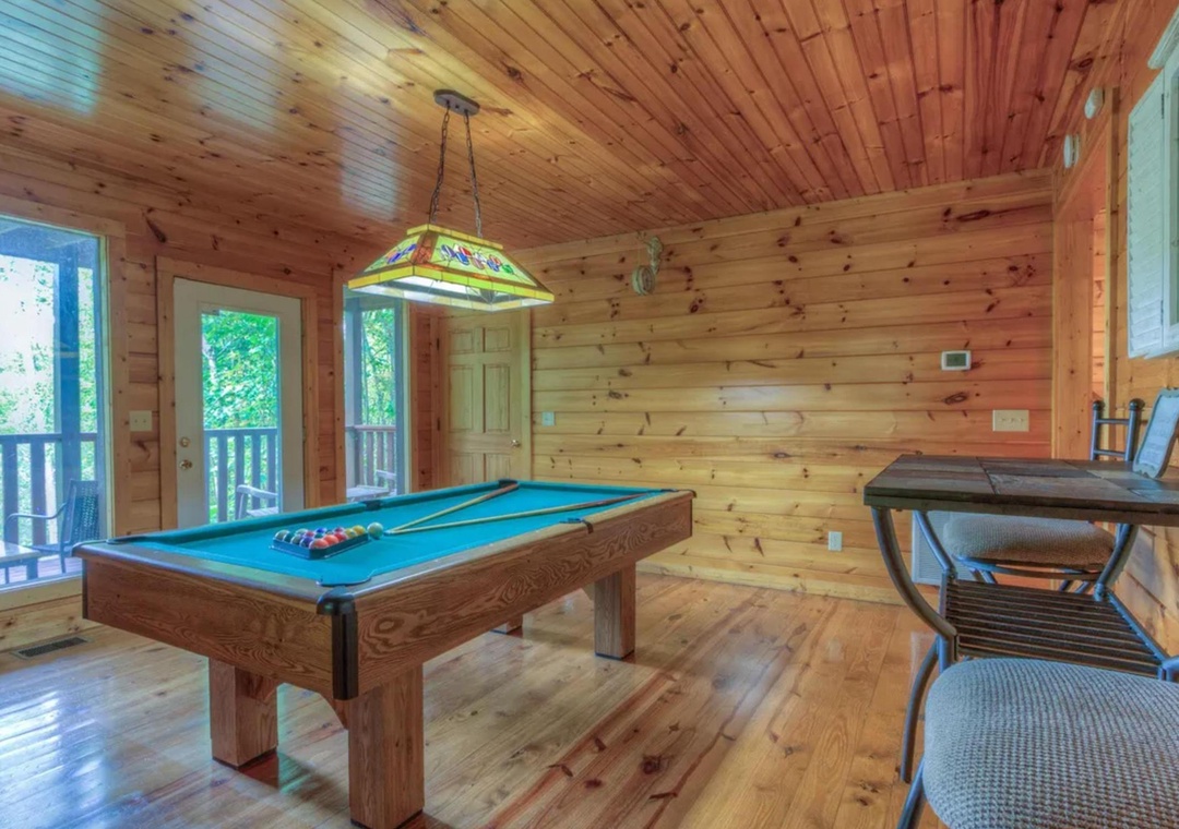 Challenge friends to a game of pool in your private game room, where rustic wood paneling creates a cozy mountain retreat feel with doors opening to a scenic deck.