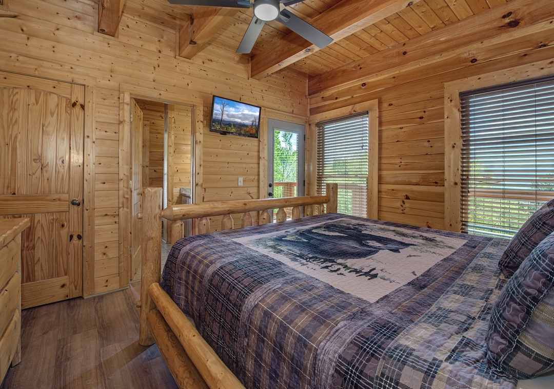 Unwind in your cozy log cabin bedroom with rustic charm, ceiling fan, and TV for peaceful mountain retreat vibes.