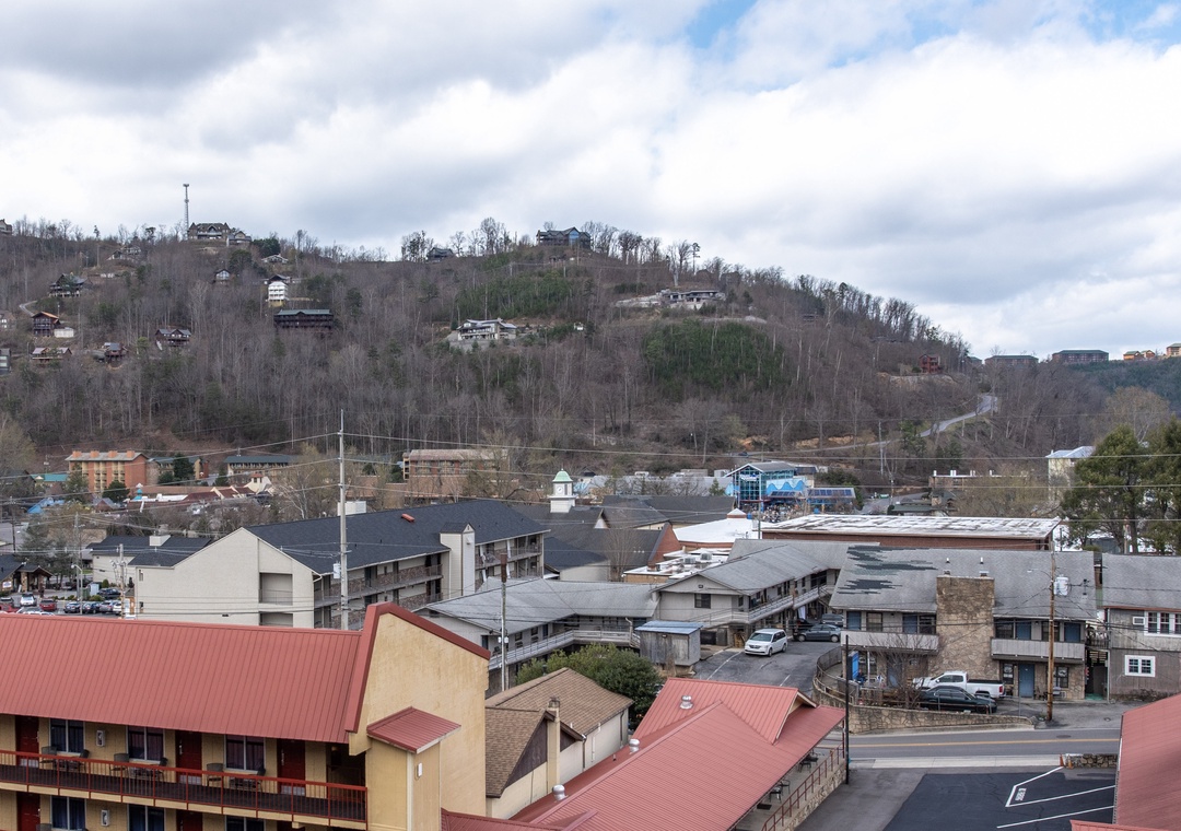 A charming hillside town spreads across rolling terrain, with residential buildings dotting the landscape under a partly cloudy sky.