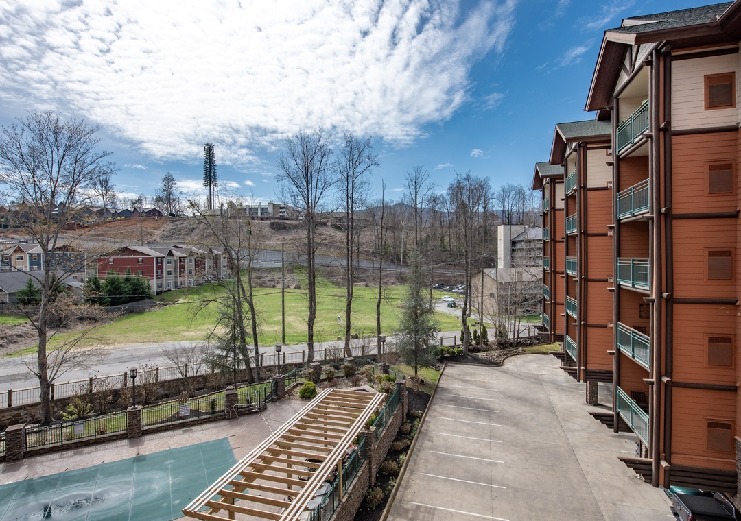 Multi-story vacation rental building with balconies overlooks green open space and surrounding residential development under partly cloudy skies.