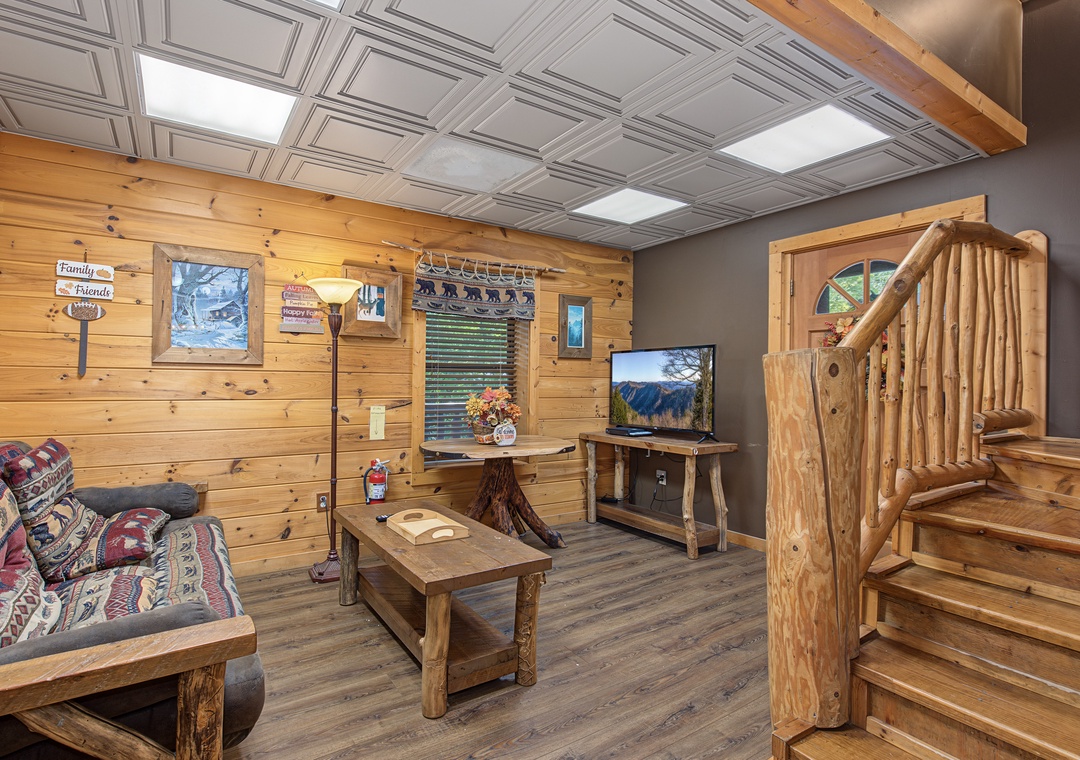 Cozy rustic living space with handcrafted log furniture, warm wood-paneled walls, and natural light streaming through skylights creates your perfect mountain retreat atmosphere.