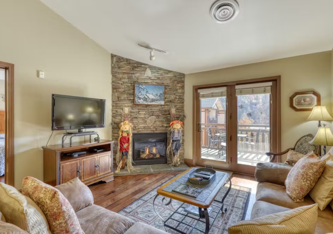 Cozy up in your mountain retreat with a stone fireplace, plush seating, and balcony views of snowy peaks.