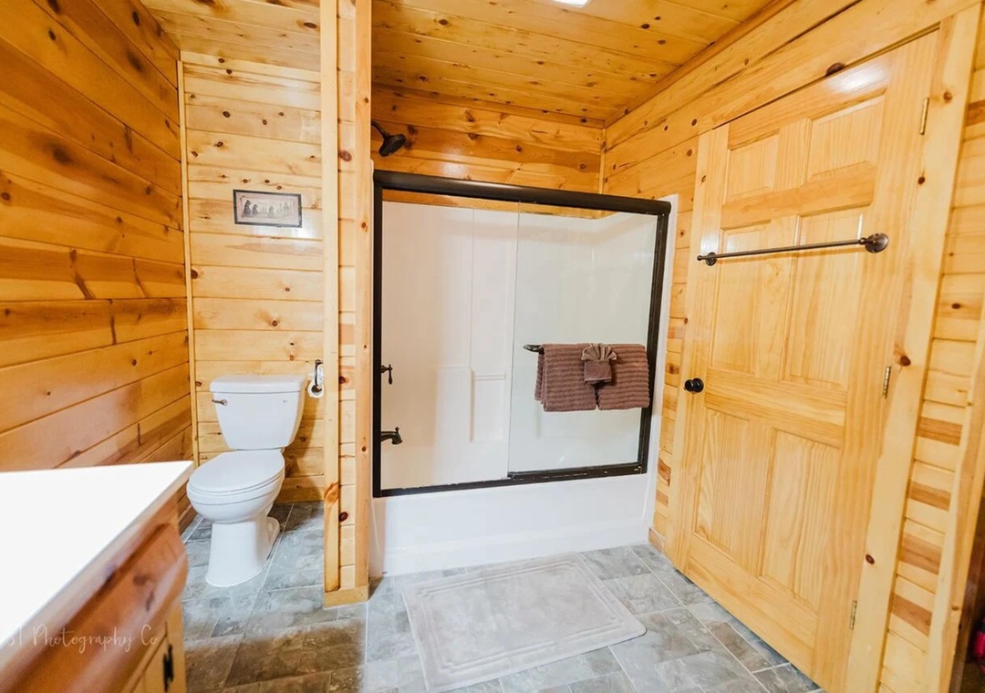 Step into your cozy cabin bathroom with warm pine walls, a tub-shower combo, and fresh towels waiting. The rustic wood and modern fixtures create a charming retreat after a day of adventure.