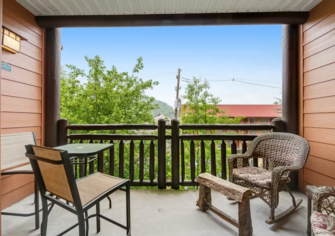 Relax on your private covered balcony with wicker seating while enjoying peaceful views of lush trees and distant mountains.