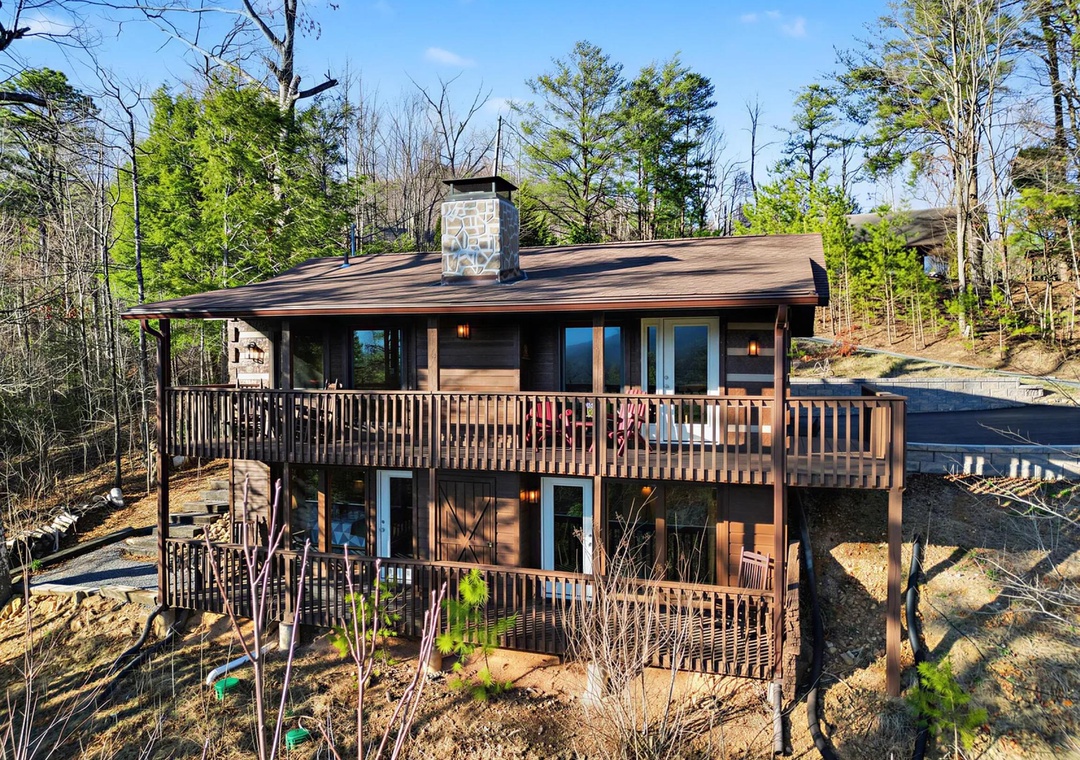 A rustic two-story cabin surrounded by peaceful woodlands offers a secluded mountain retreat with spacious wrap-around decks and a cozy stone chimney.