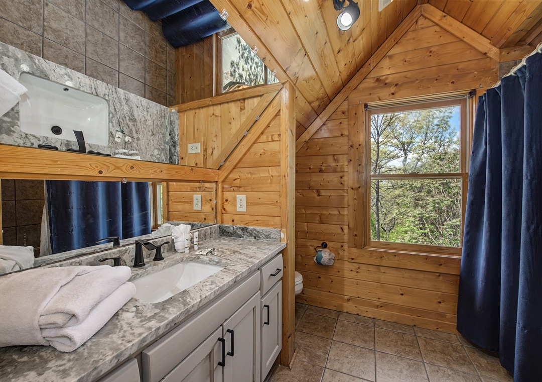 Freshen up in your rustic bathroom featuring marble countertops, warm wood walls, and nature views through the window.