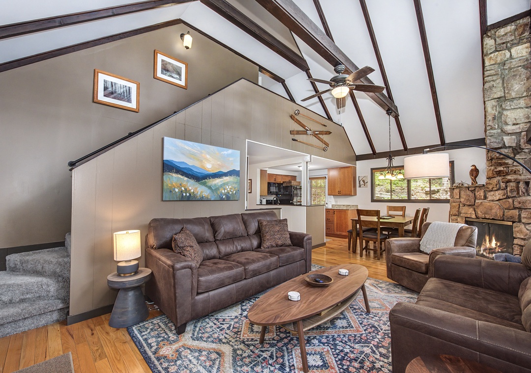Settle into this welcoming living space with soaring vaulted ceilings, leather seating around the fireplace, and an open layout that flows naturally into the dining and kitchen areas.
