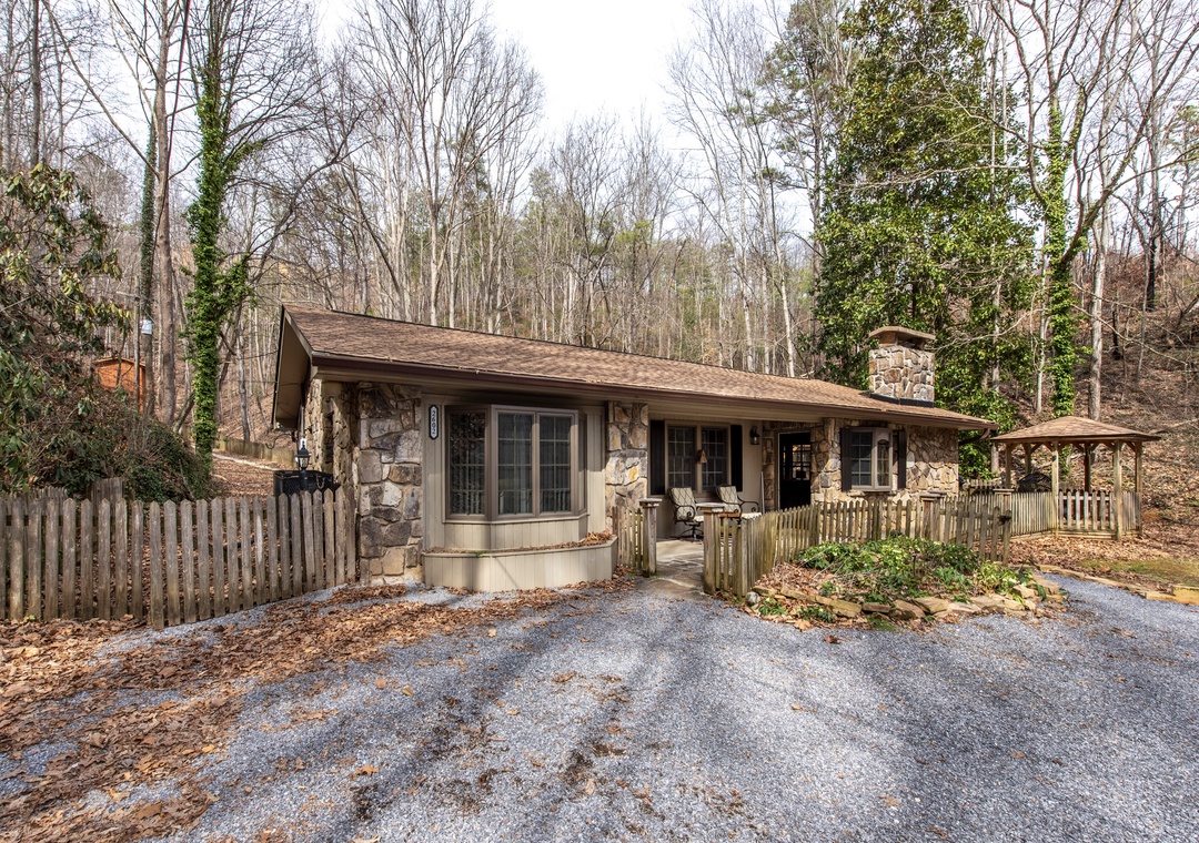 A charming stone cottage nestled among towering trees, featuring a welcoming front deck and private gazebo surrounded by peaceful woodland.