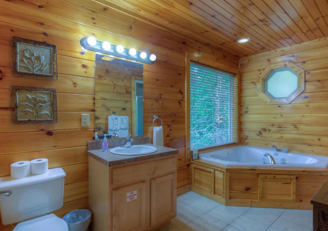 Unwind in your cabin bathroom where warm wood surrounds you and a jetted tub invites relaxation beneath forest views through the window.