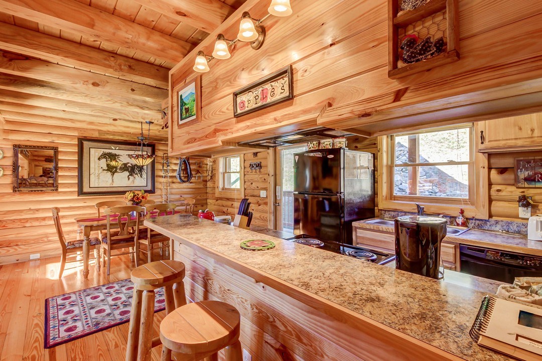 Warm wood tones surround you in this inviting kitchen and dining space, where granite countertops and modern appliances meet rustic cabin charm—perfect for preparing your morning coffee or sharing meals together.