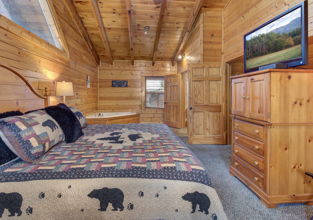 Unwind in your cozy cabin bedroom with rustic wood walls, plush bear-themed bedding, and modern TV entertainment for peaceful mountain nights.