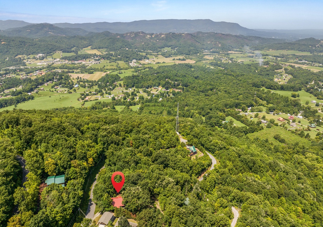 Aerial view showcasing the property's secluded location nestled among lush forests and rolling hills, with mountains rising majestically in the distance and surrounding countryside visible below.
