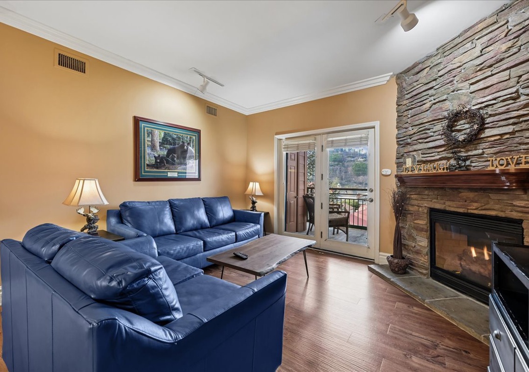 Sink into plush blue leather seating by your stone fireplace, where warm lighting and balcony access create perfect relaxation.