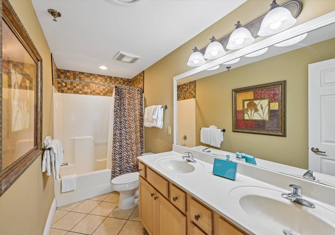 Your spacious bathroom features dual sinks, fresh towels, and a relaxing tub-shower combo with stylish tile accents for your comfort.