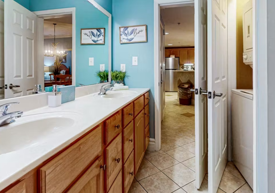 Freshen up in your spacious bathroom featuring double sinks, vibrant turquoise walls, and warm wood cabinetry that creates a welcoming retreat.