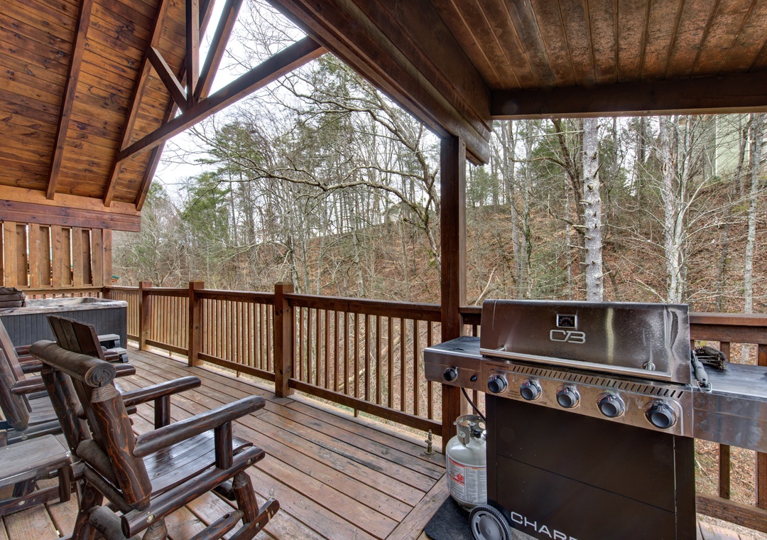 Your private covered deck overlooks peaceful woods, featuring cozy seating and a premium grill for memorable outdoor dining experiences.