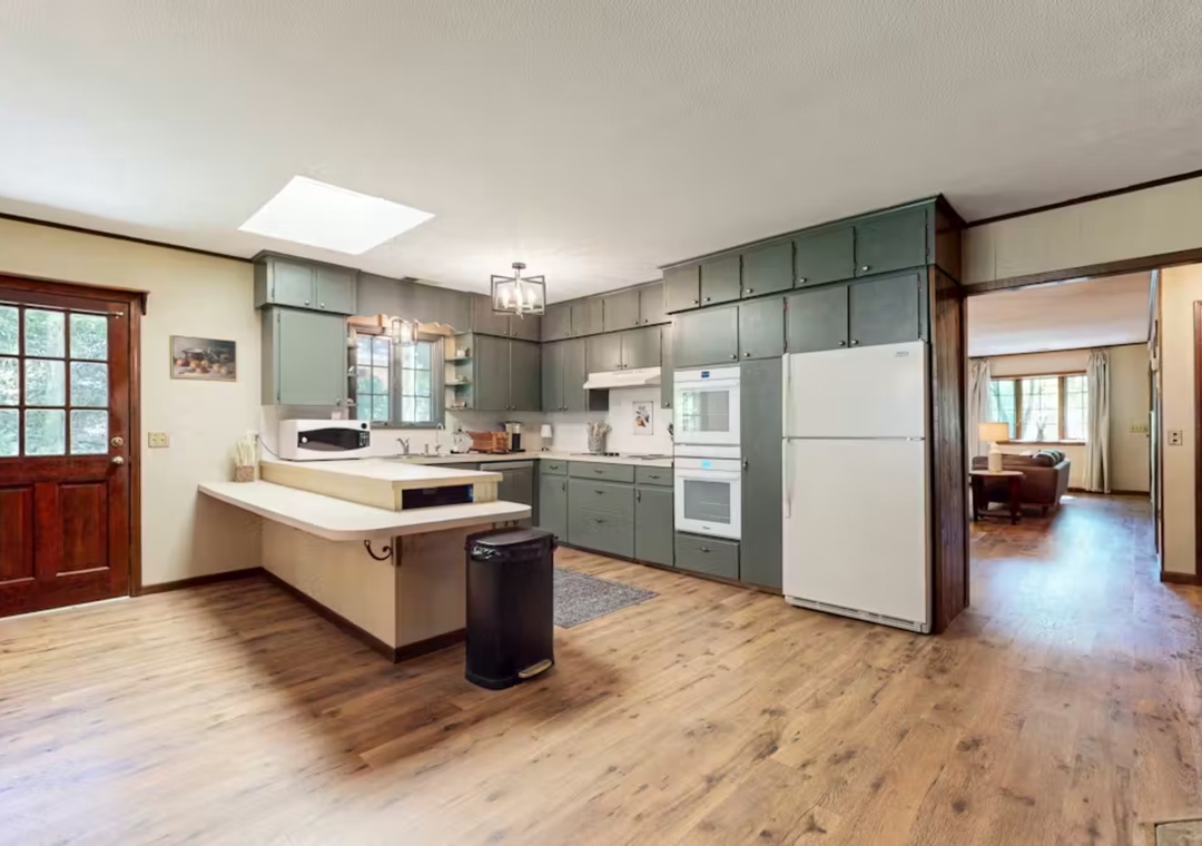 Prepare delicious meals in your spacious kitchen featuring sage-green cabinets, modern appliances, and a convenient breakfast bar for casual dining.
