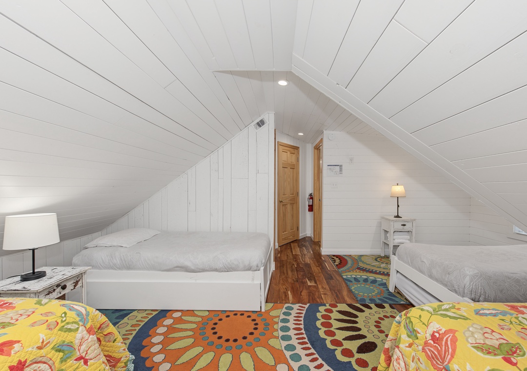 Tuck yourselves into this cozy attic retreat, where white shiplap walls embrace you beneath the sloped ceiling and cheerful rugs brighten the polished wood floors.