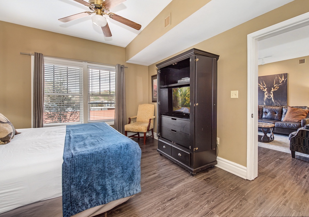 Relax in your spacious bedroom with plush bedding, entertainment center, and peaceful views through large windows.