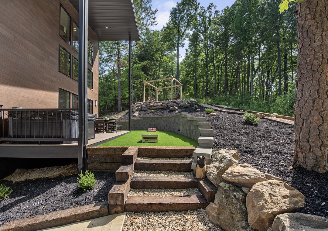 The property features terraced outdoor spaces with natural stone and timber steps, climbing structures, and a covered patio—all set within a lush forested setting.