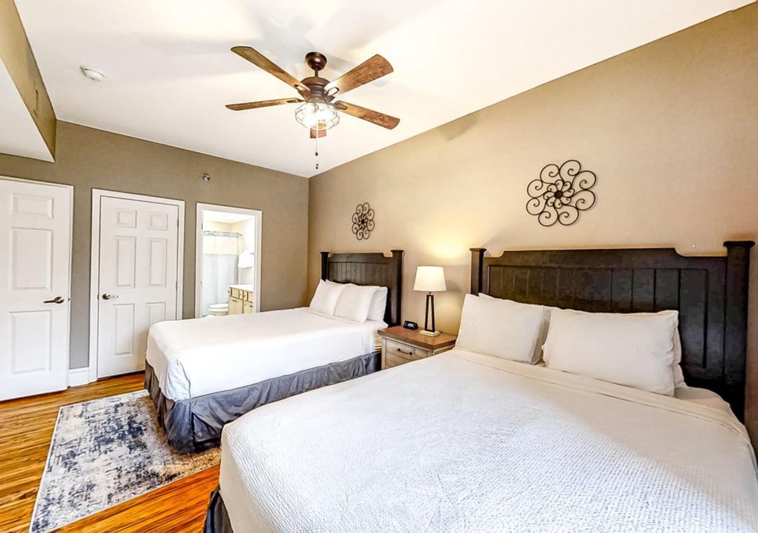 Relax in your spacious twin-bed room with rustic charm, featuring elegant dark wood headboards, crisp white linens, and a gentle ceiling fan.