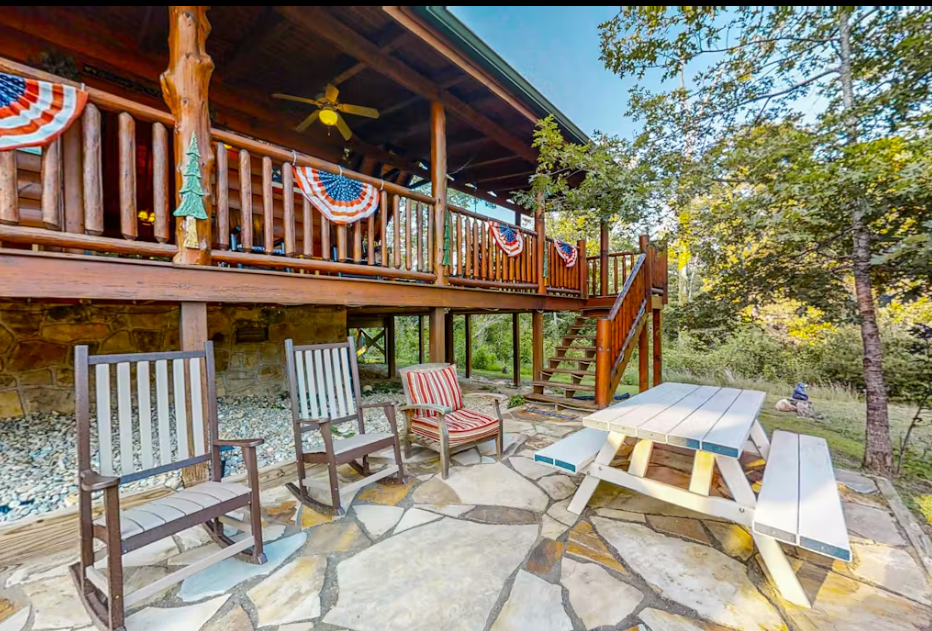 Cozy stone patio with picnic table and wooden chairs beneath your private balcony, surrounded by peaceful forest views.