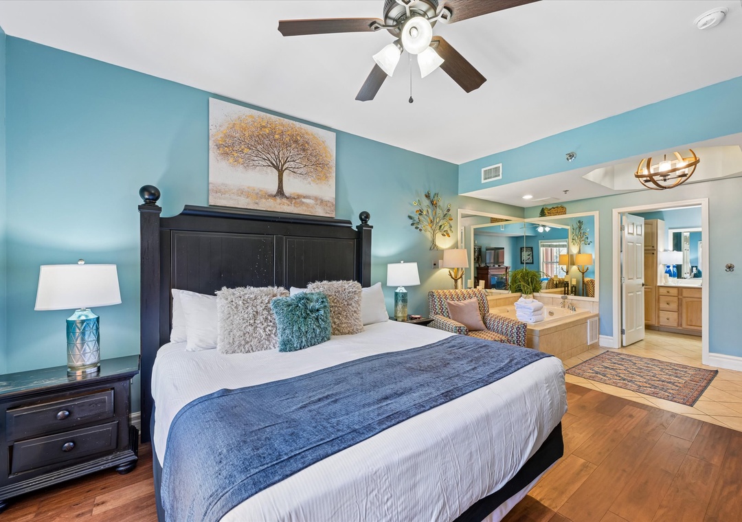 Relax in your serene king bedroom with coastal blue walls, fluffy pillows, and a spa-like ensuite visible beyond.
