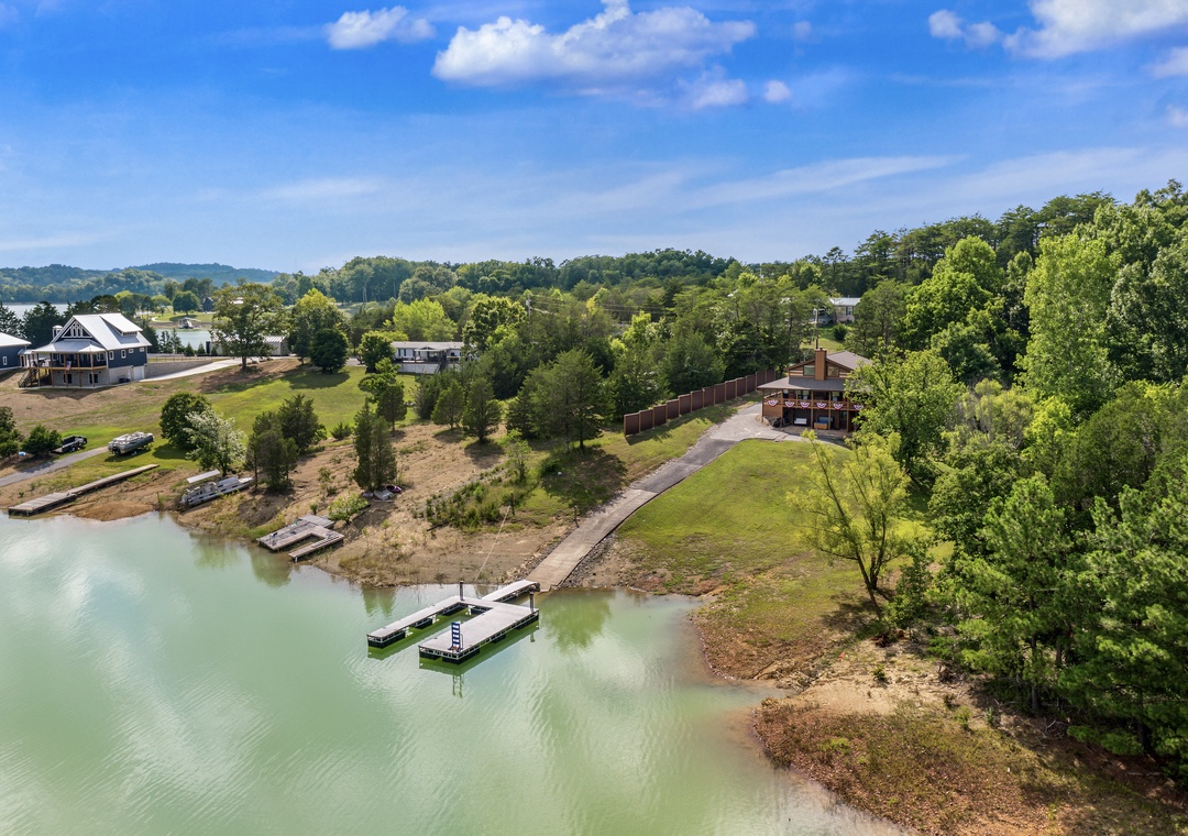 Aerial view of a lakefront property nestled among rolling hills and lush trees, featuring private docks and a peaceful shoreline setting in a scenic residential area.